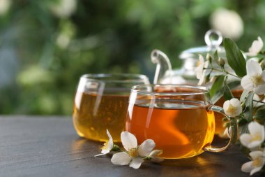 Lezzetli yasemin çayı bardakta, çaydanlık ve çiçekler siyah masada, yakın plan. Metin için boşluk