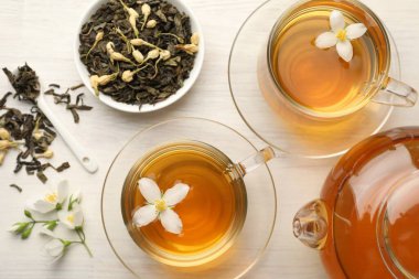 Lezzetli yasemin çayı fincanda, çaydanlıkta, kuru yapraklarda ve çiçeklerde beyaz ahşap masada, düz yerde.