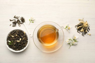 Lezzetli yasemin çayı fincanda, kuru yapraklar ve beyaz ahşap masada çiçekler, düz uzanmış