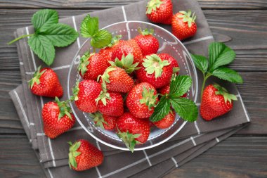 Taze olgun çilekler ve yapraklar siyah ahşap masada, düz yatıyordu.