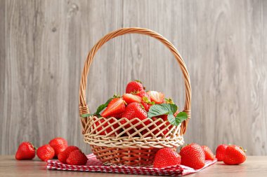 Tahta masada hasır sepetin içinde lezzetli olgun çilekler.