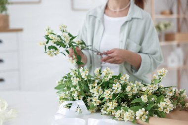 Beyaz masada yasemin dallarından buket yapan bir kadın, yakın plan.