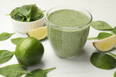 Lezzetli ıspanaklı smoothie ve malzemeler beyaz masada, yakın plan.