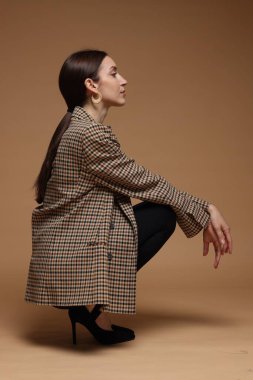 Bej arka planda şık giyinmiş güzel bir kadının tam boy portresi.