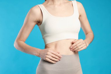 Açık mavi arka planda düz göbekli güzel bir kadın, yakın plan.