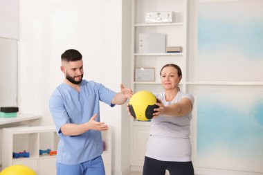 Doktor ve hasta klinikte ilaç topuyla egzersiz yapıyor.