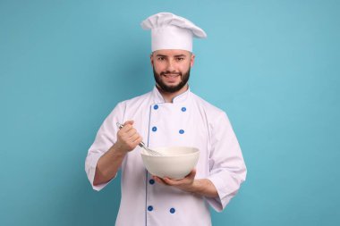 Üniformalı mutlu pastacı elinde çırpı ve kase ile açık mavi arka planda