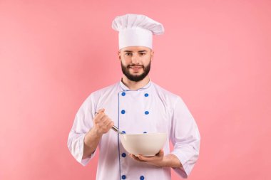 Pembe arka planda çırpı ve kase tutan üniformalı mutlu pastacı.