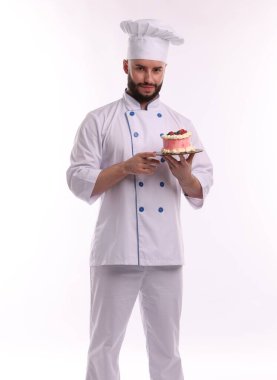 Üniformalı mutlu pastacı elinde beyaz arka planda böğürtlenli kek tutuyor.