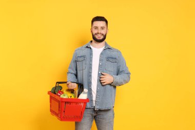 Turuncu arka planda ürünlerle dolu alışveriş sepeti olan bir adam.