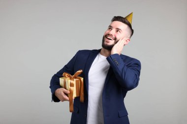 Doğum günün kutlu olsun. Gri arka planda parti şapkası ve hediye kutusu olan yakışıklı bir adam.