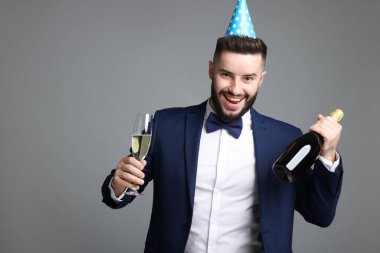 Doğum günün kutlu olsun. Gri arka planda parti şapkası ve şampanyası olan yakışıklı bir adam.