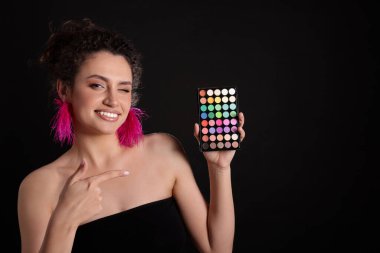 Gülümseyen kadın siyah arka plandaki parlak göz falı paletini işaret ediyor. Metin için boşluk