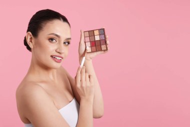 Göz farı paleti ve pembe arka planda fırçası olan bir kadın. Metin için boşluk