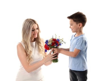 Küçük çocuk, gülümseyen annesine beyaz arka planda bir buket güzel çiçek sunuyor.