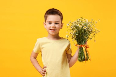 Sarı arka planda bir buket güzel papatya çiçeğiyle gülümseyen küçük çocuk