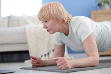 Spor giyim bölümündeki son sınıf kadın evde kalas egzersizi yapıyor, mesaj için yer var.