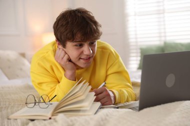 Ergen öğrenci evde laptopun yanında ders çalışırken not alıyor.