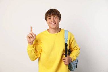 Sırt çantalı, açık gri arka planda gülümseyen genç çocuk.