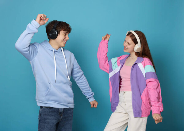 Teenage girl and boy with headphones dancing on light blue background
