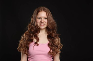 Siyah arka planda sağlıklı dalgalı saçları olan gülümseyen genç kız.