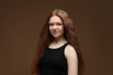 Kahverengi arka planda sağlıklı dalgalı saçlı güzel bir genç kızın portresi.