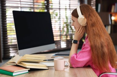 İçeride ders çalışırken kulaklıklı bir öğrenci bilgisayar kullanıyor.