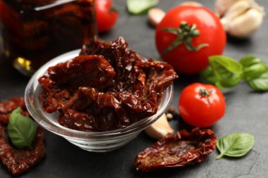 Lezzetli güneşte kurutulmuş domatesler ve taze sebzeler siyah masada, yakın plan.