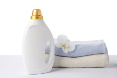 Bir şişe yumuşatıcı, üst üste yığılmış giysiler ve beyaz bir çiçek.