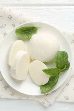 Beyaz ahşap masa üzerinde lezzetli mozzarella peyniri ve fesleğen parçaları.