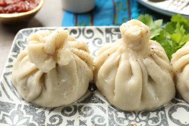 Gri masada soslu kişniş ve kişniş ile servis edilen lezzetli khinkali, yakın plan.