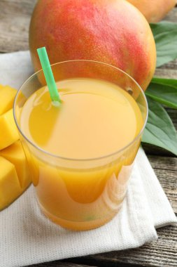 Bardakta lezzetli mango suyu, taze meyve ve ahşap masada yeşil yapraklar, yakın plan.