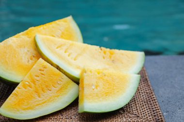 Olgun sarı karpuz parçaları hasır masada, yüzme havuzunun yanında, yakın plan.