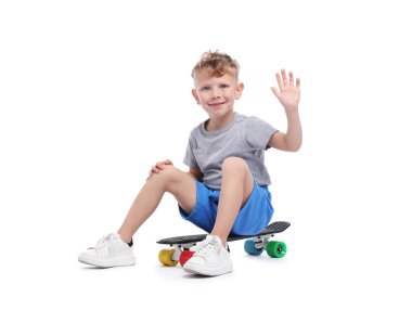 Küçük çocuk panoda oturuyor ve beyaz arka planda selamlıyor.