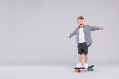 Neşeli küçük çocuk para tahtasının üzerinde duruyor ve gri arka plana başparmak gösteriyor, mesaj için yer var.