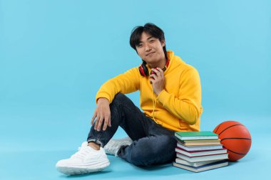 Kitapları ve açık mavi arka planda basketbol topu olan bir öğrenci.
