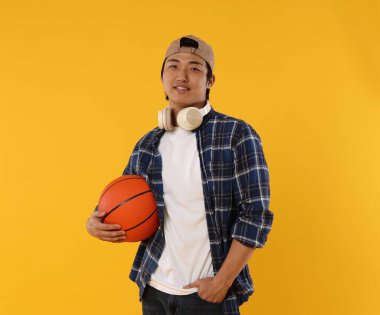 Kulaklıklı ve turuncu arka planda basketbol topu olan bir öğrenci.