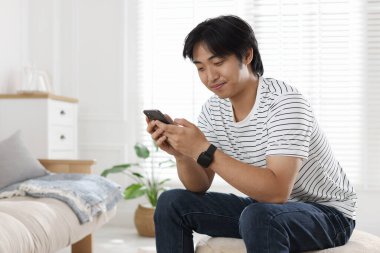 Evde akıllı telefonu olan yakışıklı Asyalı adam.