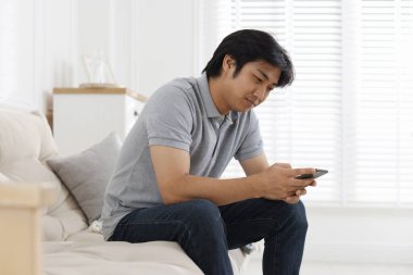 Evdeki kanepede akıllı telefonlu yakışıklı Asyalı adam.