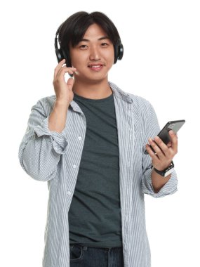 Beyaz arka planda akıllı telefonu olan kulaklıklı yakışıklı Asyalı adam.
