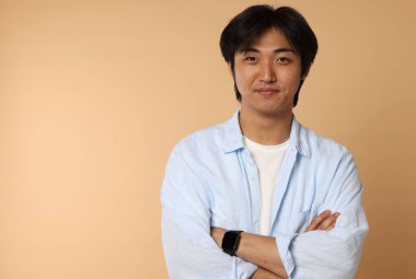 Bej arka planda çapraz kollu yakışıklı Asyalı adamın portresi. Metin için boşluk