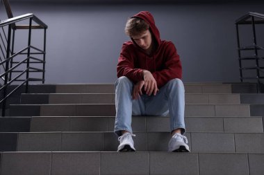 Zorbalık. Kapalı alandaki merdivenlerde üzgün genç çocuk.