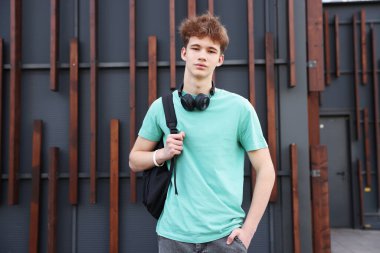 Dışarıdaki binanın yanında kulaklığı ve sırt çantası olan genç bir çocuk.