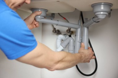 Tesisatçı, lavabonun altındaki boruları tamir ediyor. Kapalı.