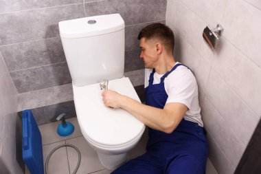 Profesyonel tesisatçı tuvalette klozet tamir ediyor.
