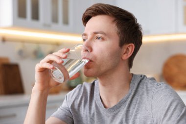 Adam mutfakta camdan su içiyor.