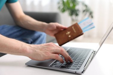 Pasaportu ve uçuş biletleri olan bir adam masadaki bilgisayarı kullanıyor, yakın plan.