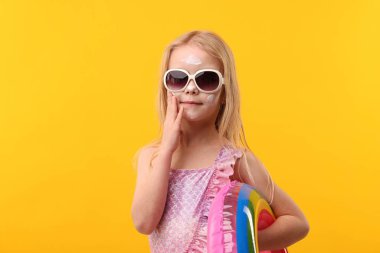 Yüzünde sarı arka planda güneş kremi olan tatlı küçük bir kız.