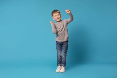 Mutlu küçük çocuk açık mavi arka planda dans ediyor