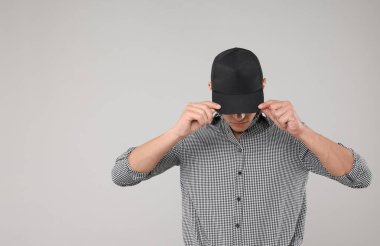 Açık gri arka planda şık siyah beysbol şapkası giyen genç adam, mesaj için yer var.